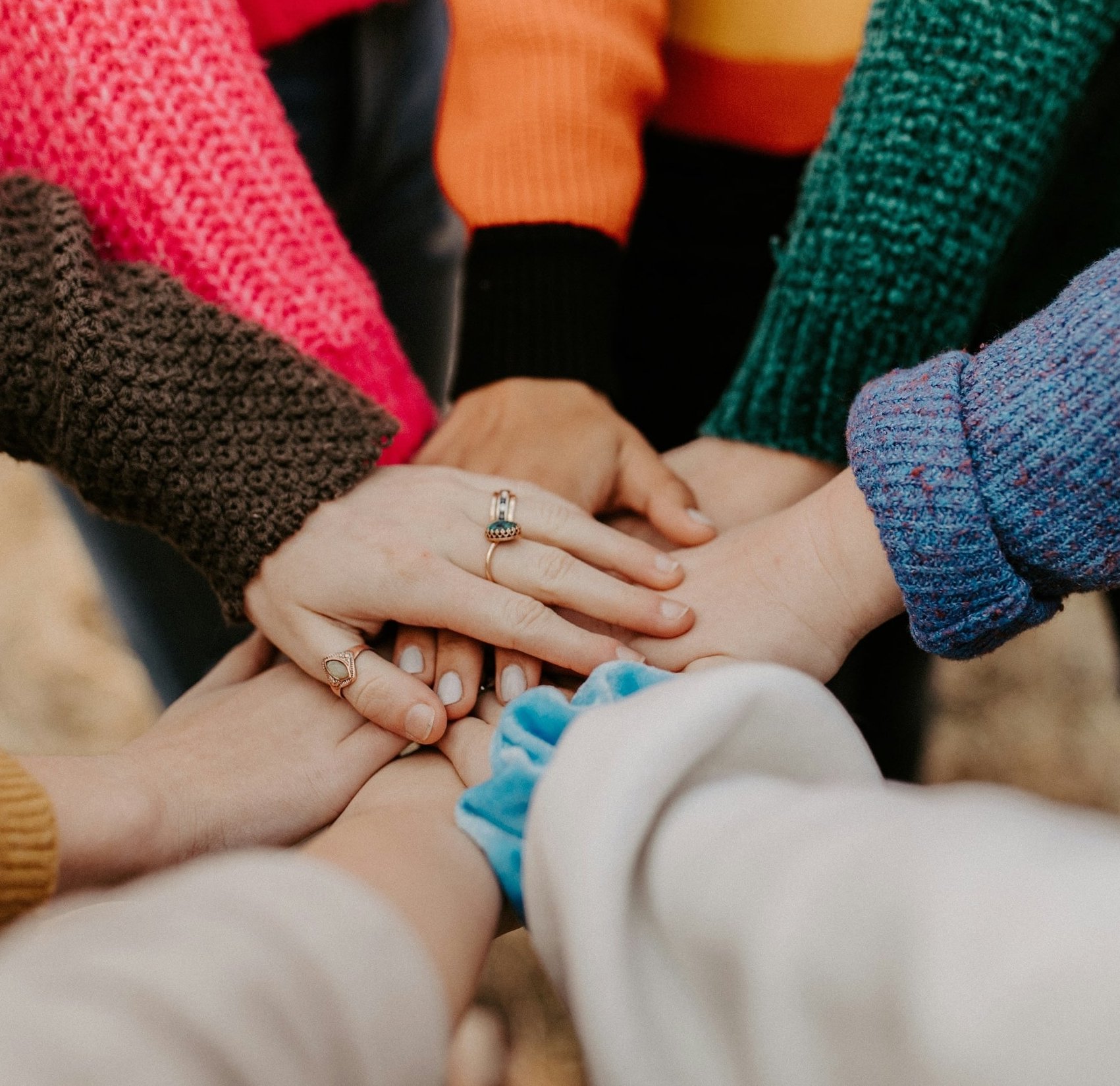 A close-up shot of several hands with rings stacked on top of each other, wearing colorful sweaters, showing unity and togetherness.