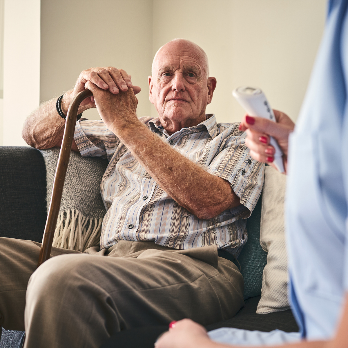 Elderly man with a cane and a nurse holding a thermometer to take his temperature.